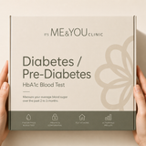 A person's hands holding a square product box for the 'It's Me & You Clinic' Diabetes / Pre-Diabetes HbA1c Blood Test. The box is beige with dark gray text and a dark gray bottom strip, set against a matching beige background.