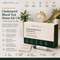 Promotional graphic for the i'm ME & YOU Clinic Cholesterol Blood Test Home Kit UK. The kit includes a white and gold test kit box, a white and gold pen, and a small card, all displayed against a dark green and beige background with feature icons and a gold heart graphic.