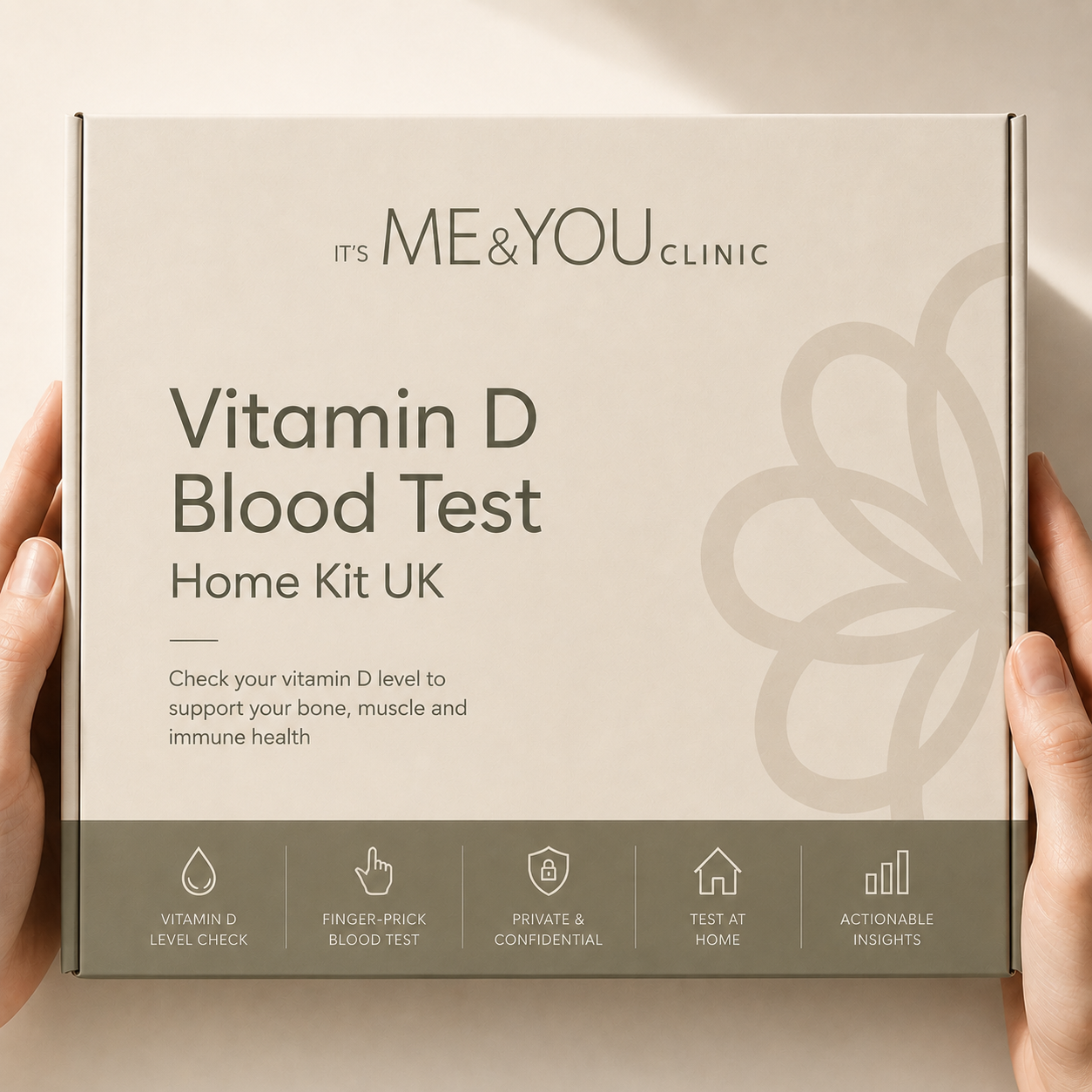 A person's hands holding a square product box for the 'It's Me & You Clinic Vitamin D Blood Test Home Kit UK'. The box is beige with dark gray text and a dark gray bottom banner with feature icons.